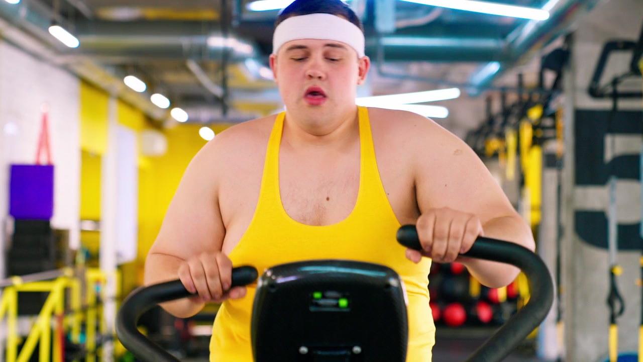 モダンなジムでエアロバイクに乗って運動する体格の大きな男性。
