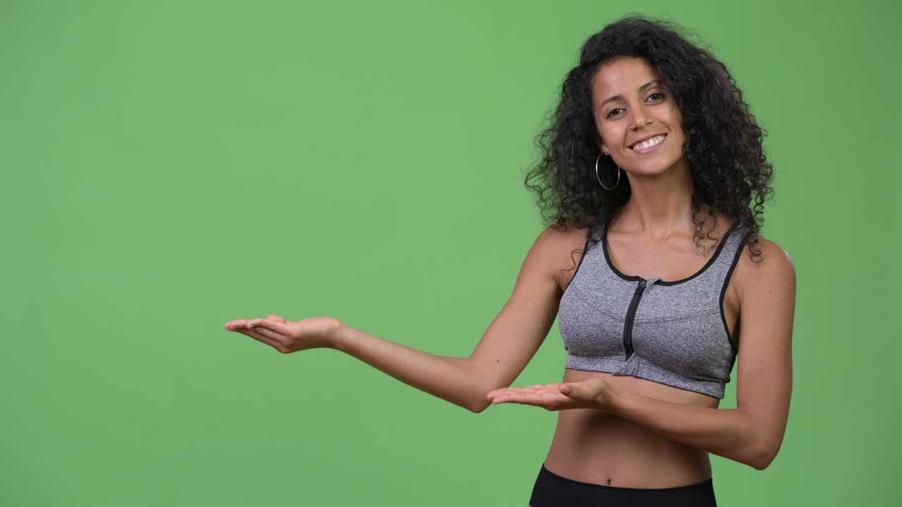Young beautiful Hispanic woman with gym clothes showing something