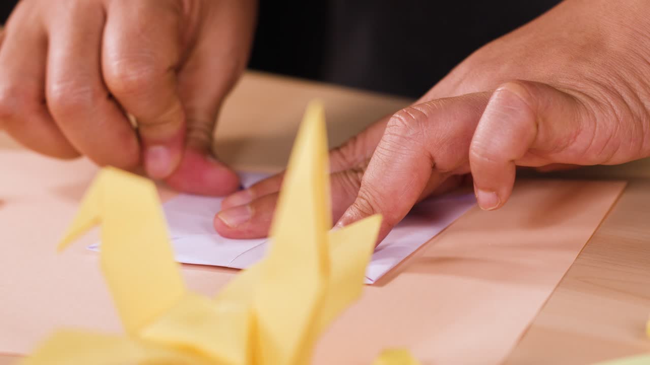 Close-up shot of hands carefully folding purple paper to create an origami crane on table