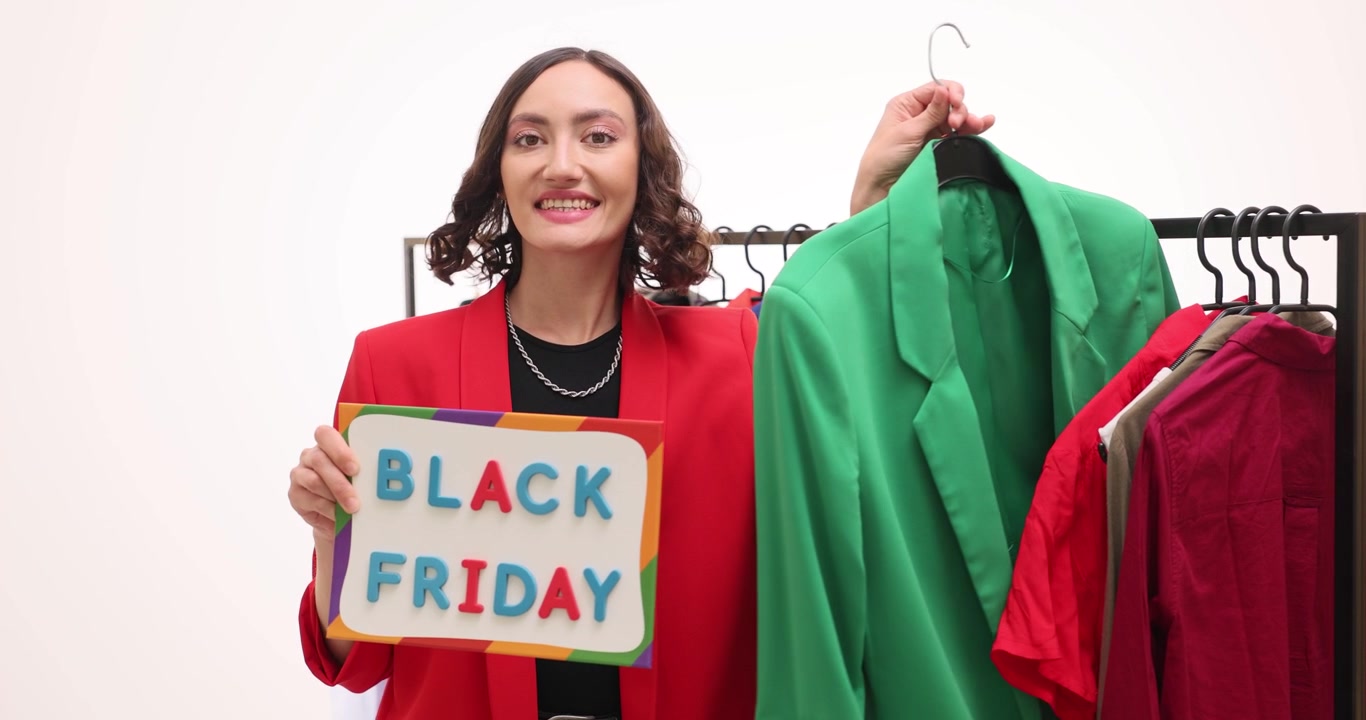 Donna allegra tiene un cartello con la scritta Black Friday vicino a un appendiabiti