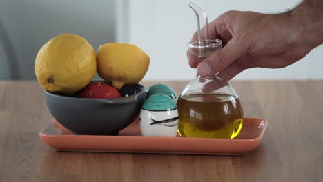 pouring olive oil with fresh fruit bowl in background