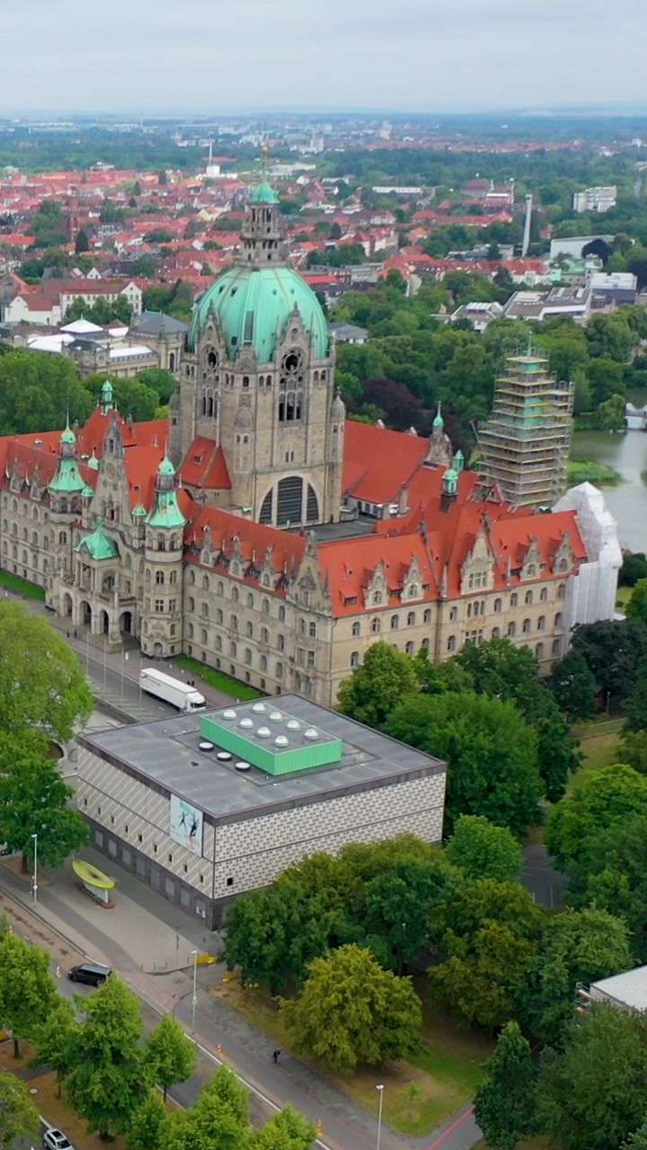 Ripresa aerea verticale cinematografica dello storico Nuovo Municipio (Neues Rathaus) ad Hannover, Germania, circondato da alberi verdi lussureggianti e dal paesaggio urbano
