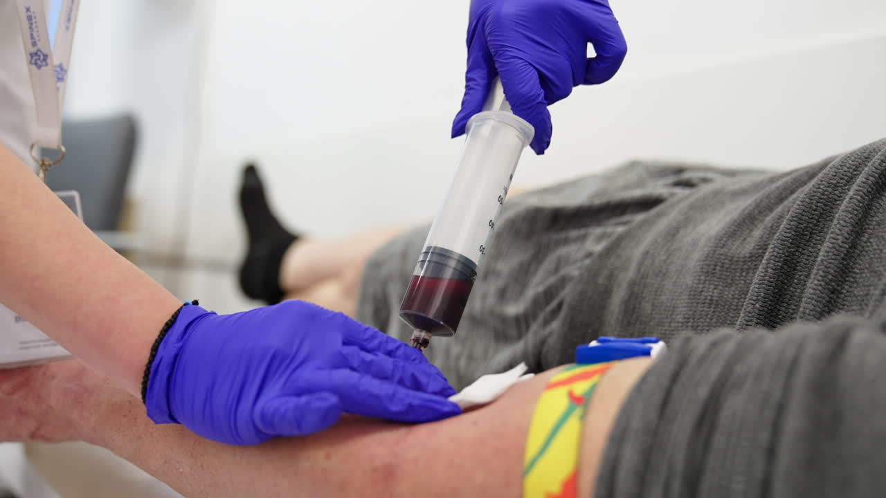 Taking vein blood with a large syringe. Medic in blue gloves gets blood from a male patient lying on the couch. Close up.