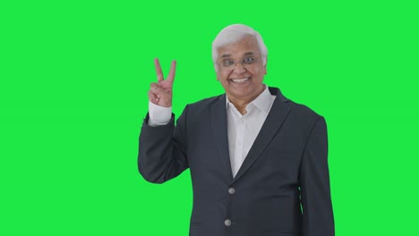 Happy-Indian-senior-journalist-pointing-at-green-screen-showing-victory-sign