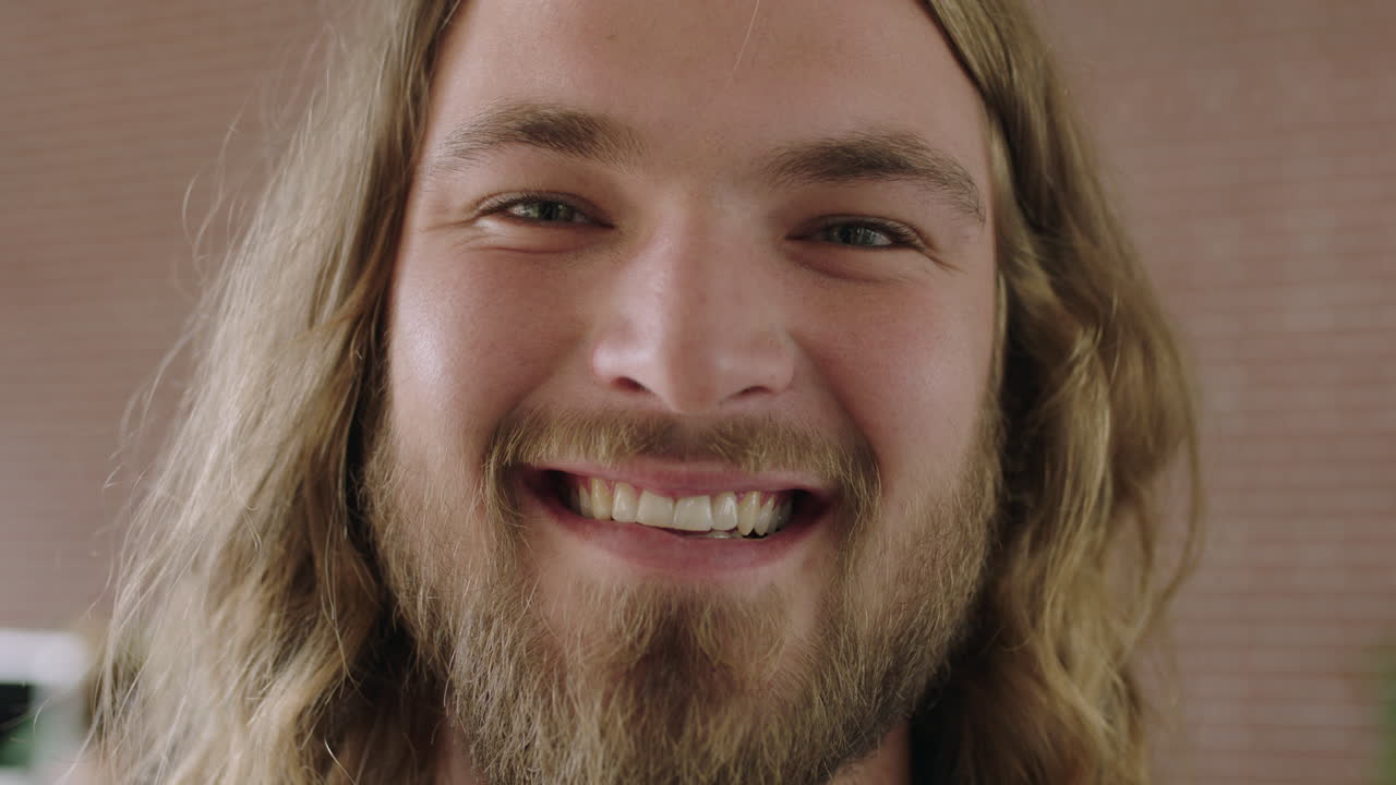 retrato en primer plano de un atractivo hombre joven barbudo sonriendo alegremente a la cámara confiado hombre caucásico de pelo largo
