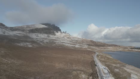 Isla-De-Skye,-Escocia,-Costa-Cerca-Con-Vistas-A-Los-Picos-Nevados-Del-Viejo-De-Las-Montañas-Storr-Bajo-Un-Cielo-Azul,-Y-Una-Carretera-Junto-A-La-Costa