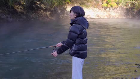 side portrait of a woman standing by the riverbank, catching fish with fishing rod