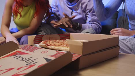 studio shot of young gen z friends sitting on sofa with home delivery takeaway pizza