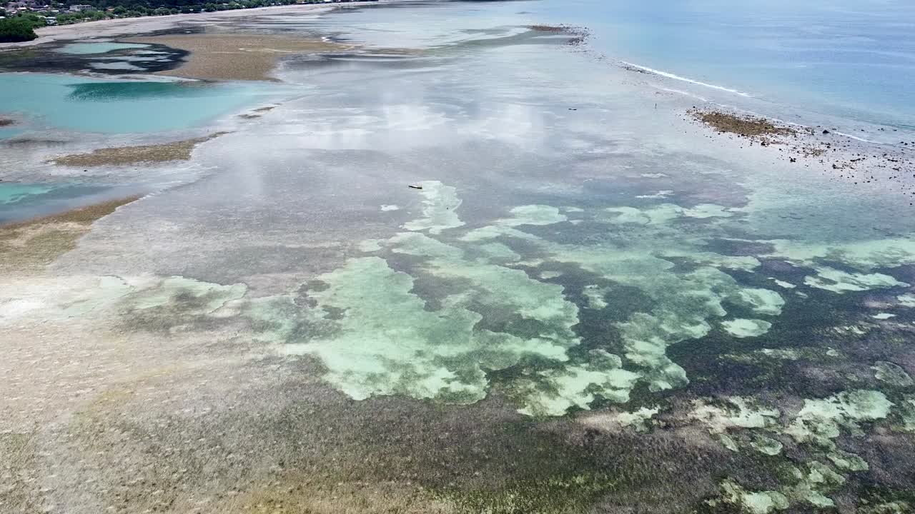 drone aéreo sobre una canoa de pesca tradicional en solitario durante la marea baja con barras de arena, arrecifes de coral y aguas cristalinas en una isla paradisíaca tropical
