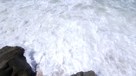 Weiße-Welle,-Die-Aus-Dem-Türkisblauen-Meer-Kommt-Und-Auf-Klippen-Am-Strand-Plätschert,-Schöne-Folgebewegungsaufnahme