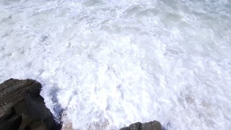 White-wave-coming-from-blue-turquoise-sea-and-splashing-on-cliffs-at-beach,-beautiful-follow-motion-shot