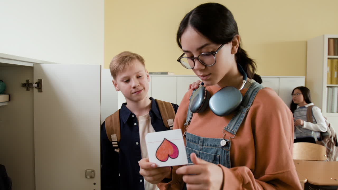 Students in a school hallway exchanging a handmade card with a heart and receiving a positive reaction