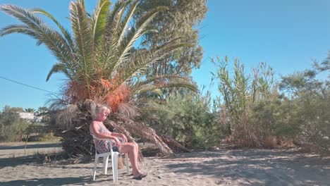 female holiday maker sits on sandy beach under palm tree