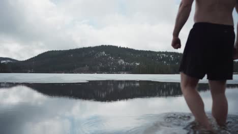 man walks to the water to swim with mountain landscape