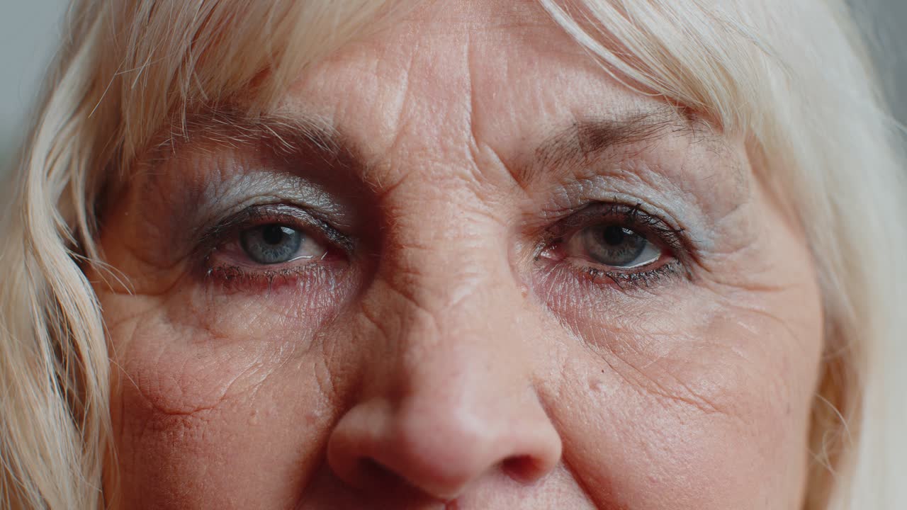 Extreme closeup macro portrait of wrinkled face old senior beautiful woman eyes looking at camera
