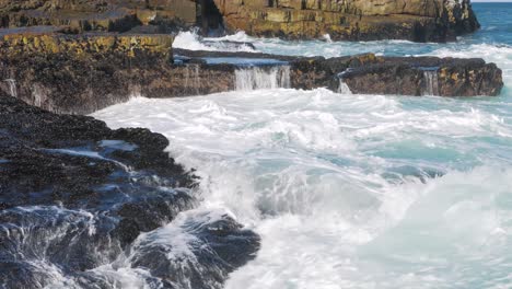 Seawater-streaming-down-face-of-rocks-on-coastline-covered-with-small-black-mussels