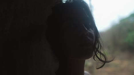 young woman looking out from a shadowy room, soft focus on her contemplative face, natural light background