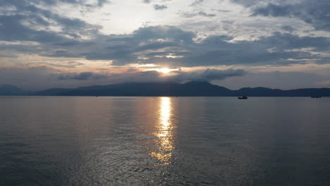 Beautiful-Vietnamese-landscape-of-a-golden-sunset-reflecting-over-the-ocean-with-mountains-and-traditional-fishing-boat