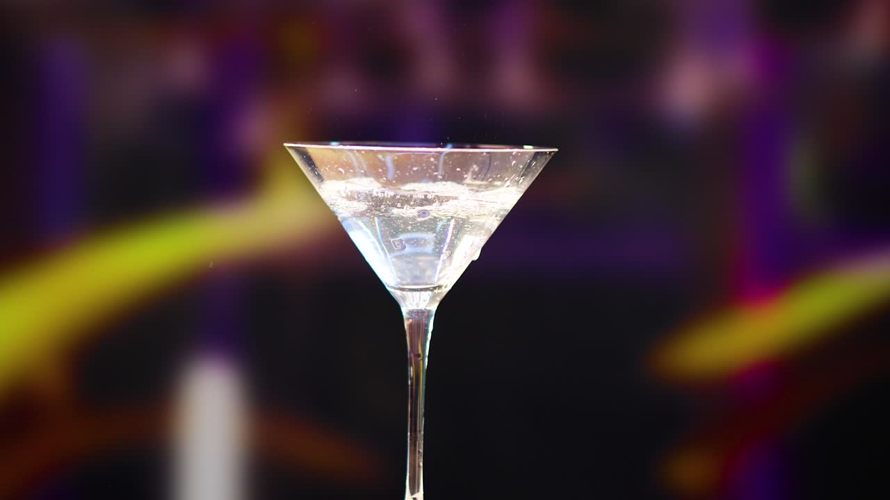 A martini is crafted with precision, garnished with a lemon twist, against a colorful, blurred background
