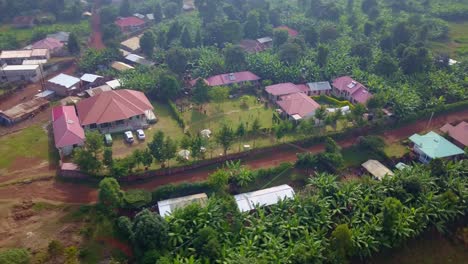 Fast orbit drone shot of a red-roofed guesthouse complex surrounded by banana trees and vegetation in Kapchorwa, Uganda, with a courtyard used for sports and social gatherings.