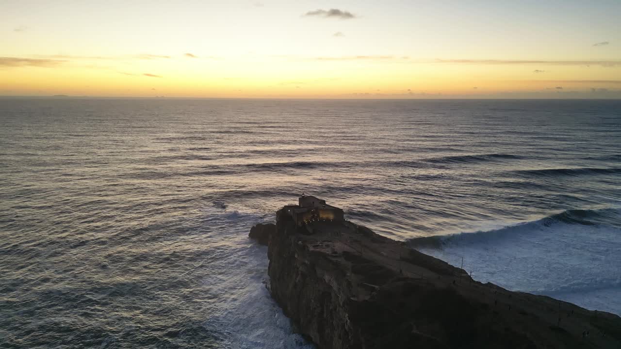 Dramatic sunset over the ocean with waves crashing near the Farol de Nazaré in Portugal
