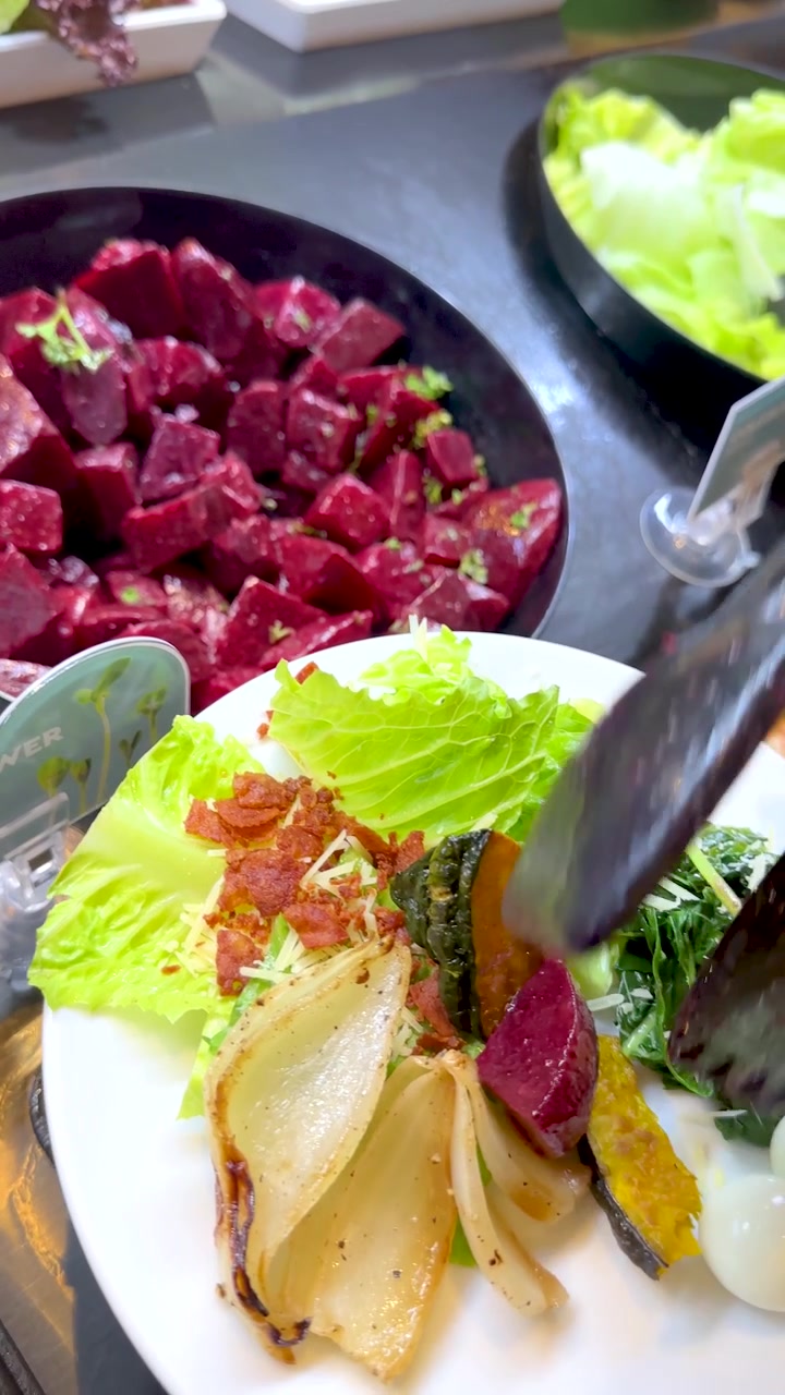 Un primo piano mostra una mano che usa delle pinze per aggiungere barbabietola a un piatto di insalata.
