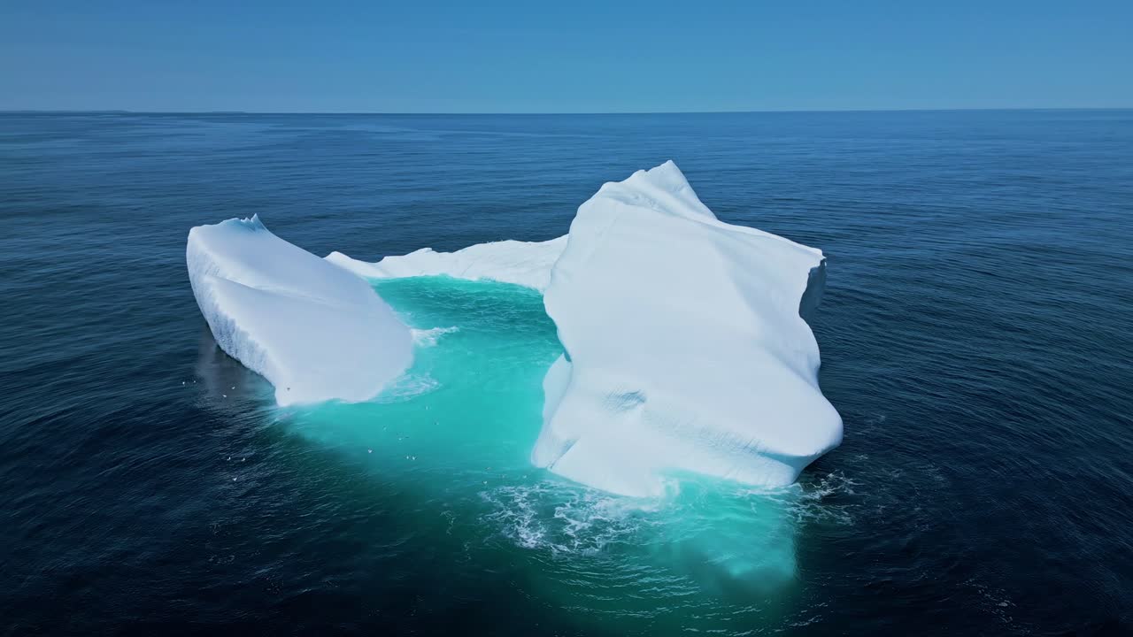 Aerial footage of a large iceberg off Flatrock, Newfoundland, featuring vivid turquoise meltwater in calm Atlantic waters.