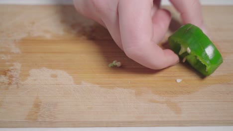 hands scoops up green pepper slices from wooden cutting board, closeup