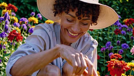 a woman in a sun hat smiles while tending to colorful flowers in a garden