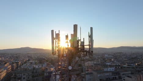 cell tower at sunset with sunrays between antennas and city in the background