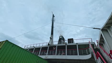 a truck with a green container boards a ferry under cloudy skies in koh samui, thailand. the scene captures movement and industrial activity