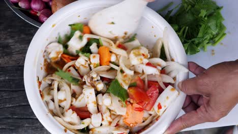 mixing squid and vegetable dish with spoon for serving, top down shot