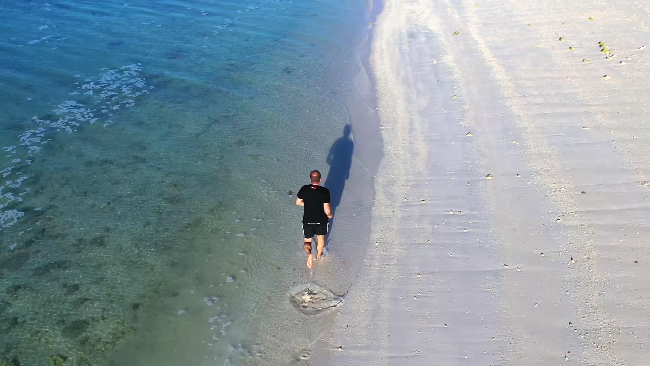 Man jogging on white sand and clear water alone at tropical beach of Boracay. Aerial dolly