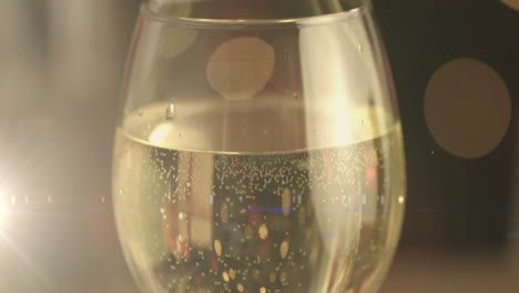 digital composition of golden spots of light against wine glass on wooden surface