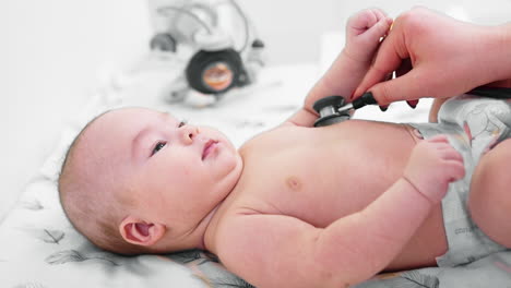 beautiful toddler being examined by the pediatrician. doctor puts stethoscope to baby's chest and belly and shows a toy to distract from examination.