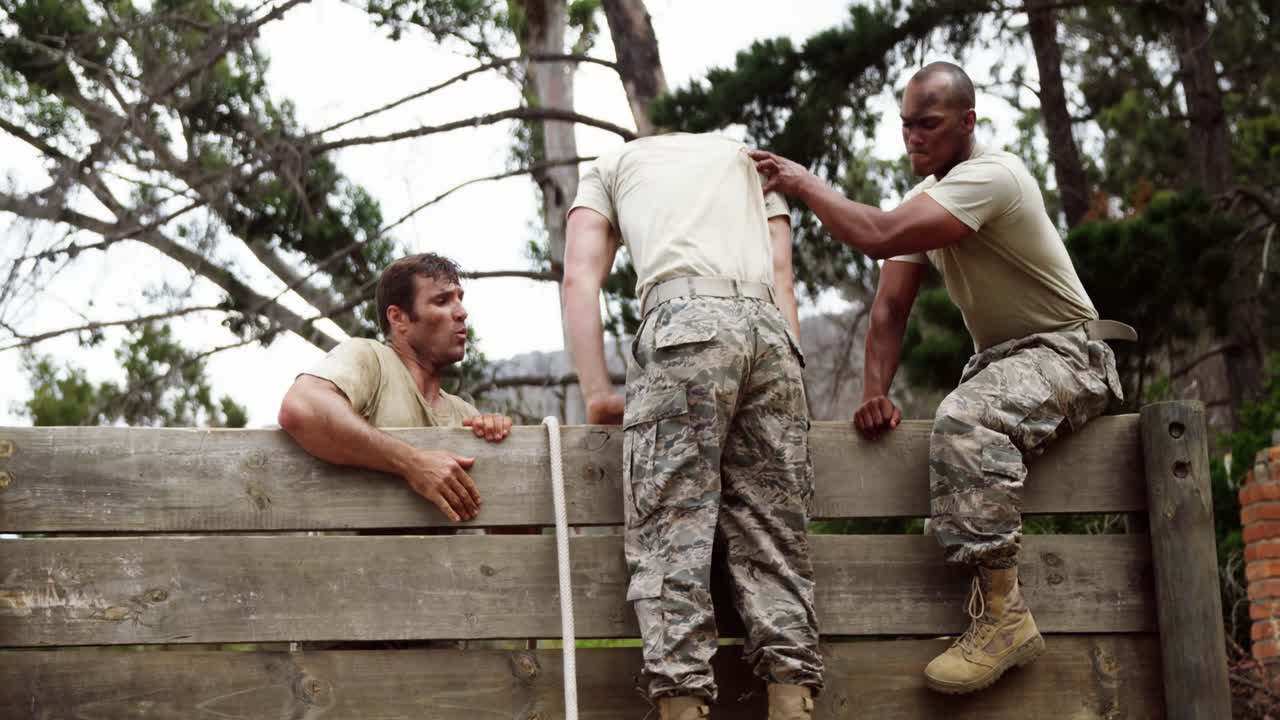 soldados masculinos ayudando a su compañero de equipo a escalar una pared de madera 4k