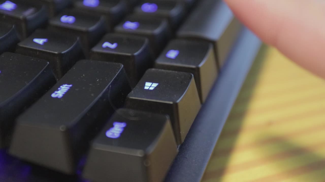 mano presionando una sola tecla en un teclado negro ligeramente polvoriento con teclas retroiluminadas azules