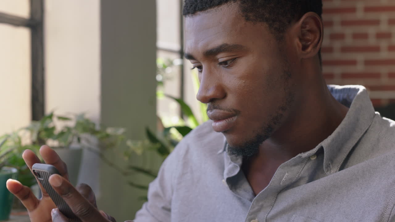 portrait attractive african american man using smartphone drinking coffee at home enjoying relaxed morning browsing messages networking texting social media sharing lifestyle online close up