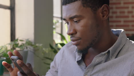 portrait attractive african american man using smartphone drinking coffee at home enjoying relaxed morning browsing messages networking texting social media sharing lifestyle online close up