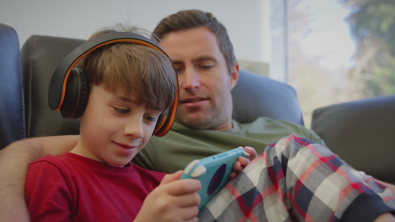 padre con su hijo usando auriculares inalámbricos jugando a un juego de computadora en un dispositivo portátil - filmado en cámara lenta