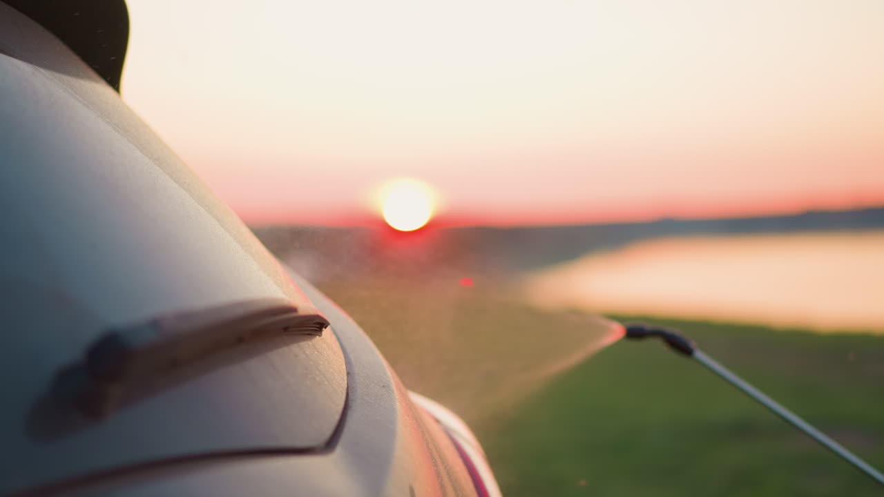 강변에서 물 스프레이로 차를 청소하는 주인이 빨간색의 호수 연안에서 수동으로 자동차를 습니다.