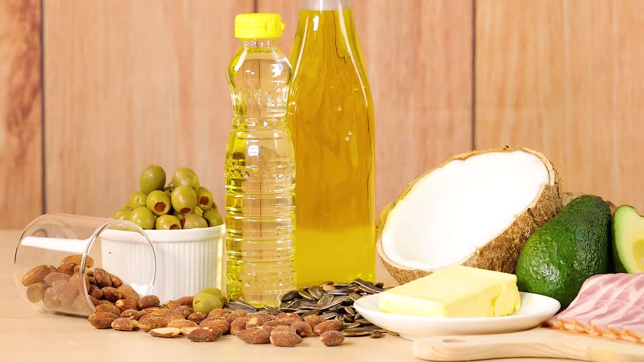 A variety of healthy fats and oils arranged on a wooden surface, including avocados, coconut, and olive oil