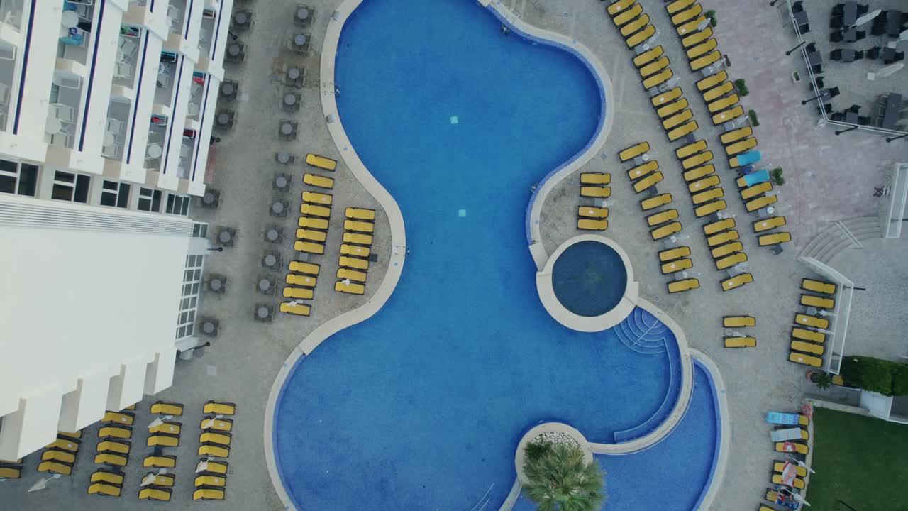 A top-down drone shot of a pool with clockwise rotation, and downward-to-upward direction, at a hotel