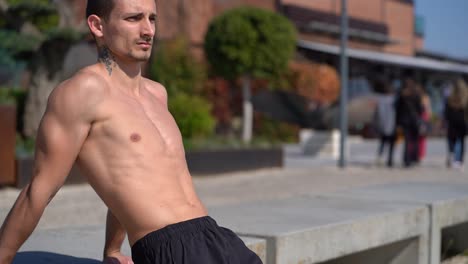 hombre atlético tatuado entrenando en el terraplén en un día soleado