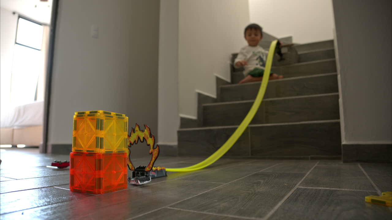 joven niño latino mexicano jugando en las escaleras de su casa con sus juguetes de coche usando una larga pista y bloques de imán