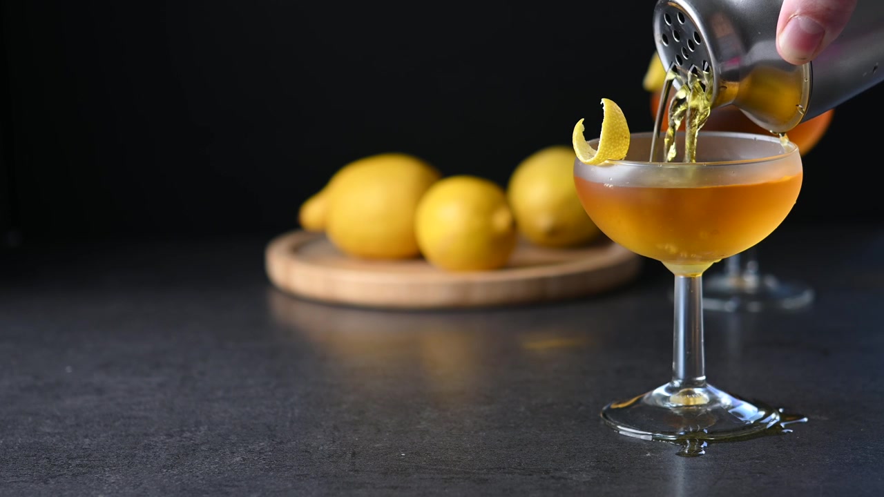 Barman che versa un cocktail ambrato in un bicchiere coupe con guarnizione al limone