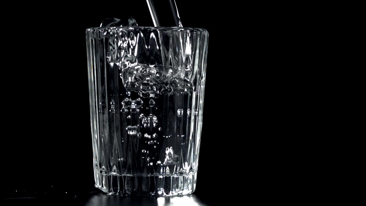 Slowmotion hældning af vand i et glas på sort baggrund