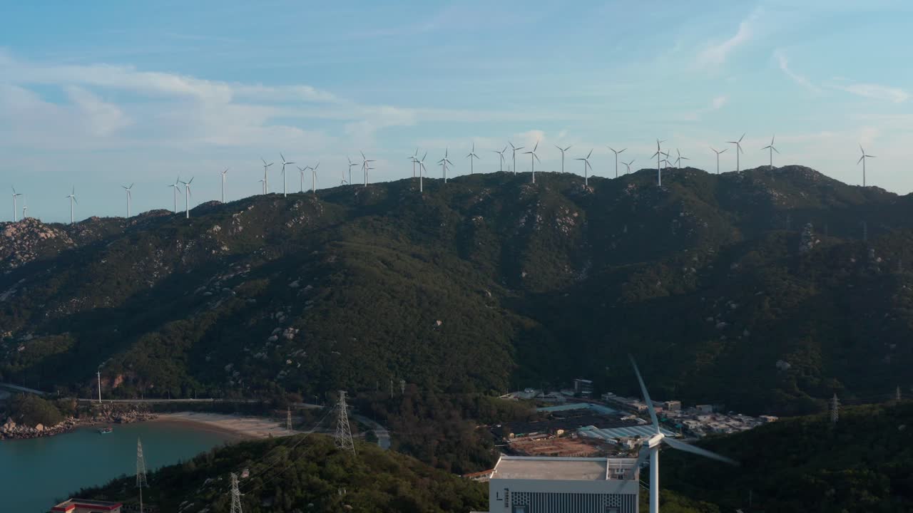 granja de turbinas eólicas en la cima de la cresta de la montaña junto al mar y planta de energía en su parte inferior en una tarde soleada