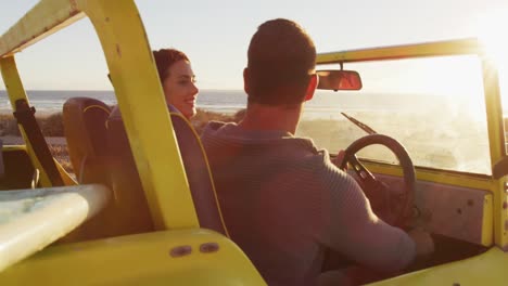 feliz pareja caucásica sentada en un buggy de playa junto al mar hablando