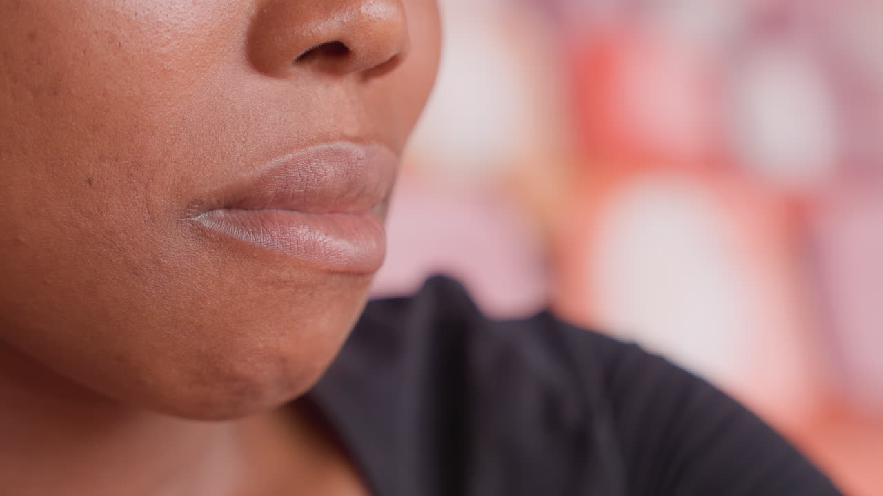 Donna di colore di profilo con labbra screpolate e pelle desquamata, sfondo tenue, espressione contemplativa, atmosfera da caffè urbano. Primo piano spontaneo sulla salute, un problema di cura della pelle catturato per sensibilizzazione.